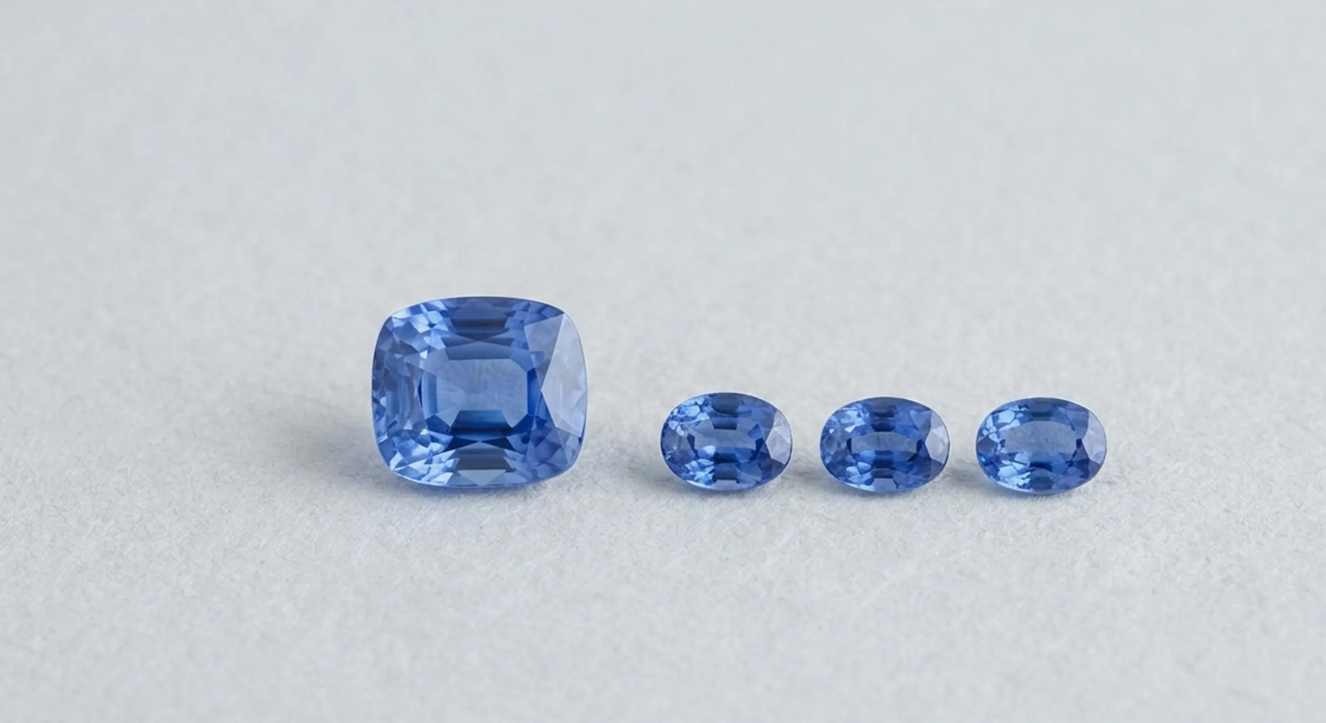 A single cornflower-blue Ceylon sapphire with a graduated row of blue sapphires on a pale backdrop
