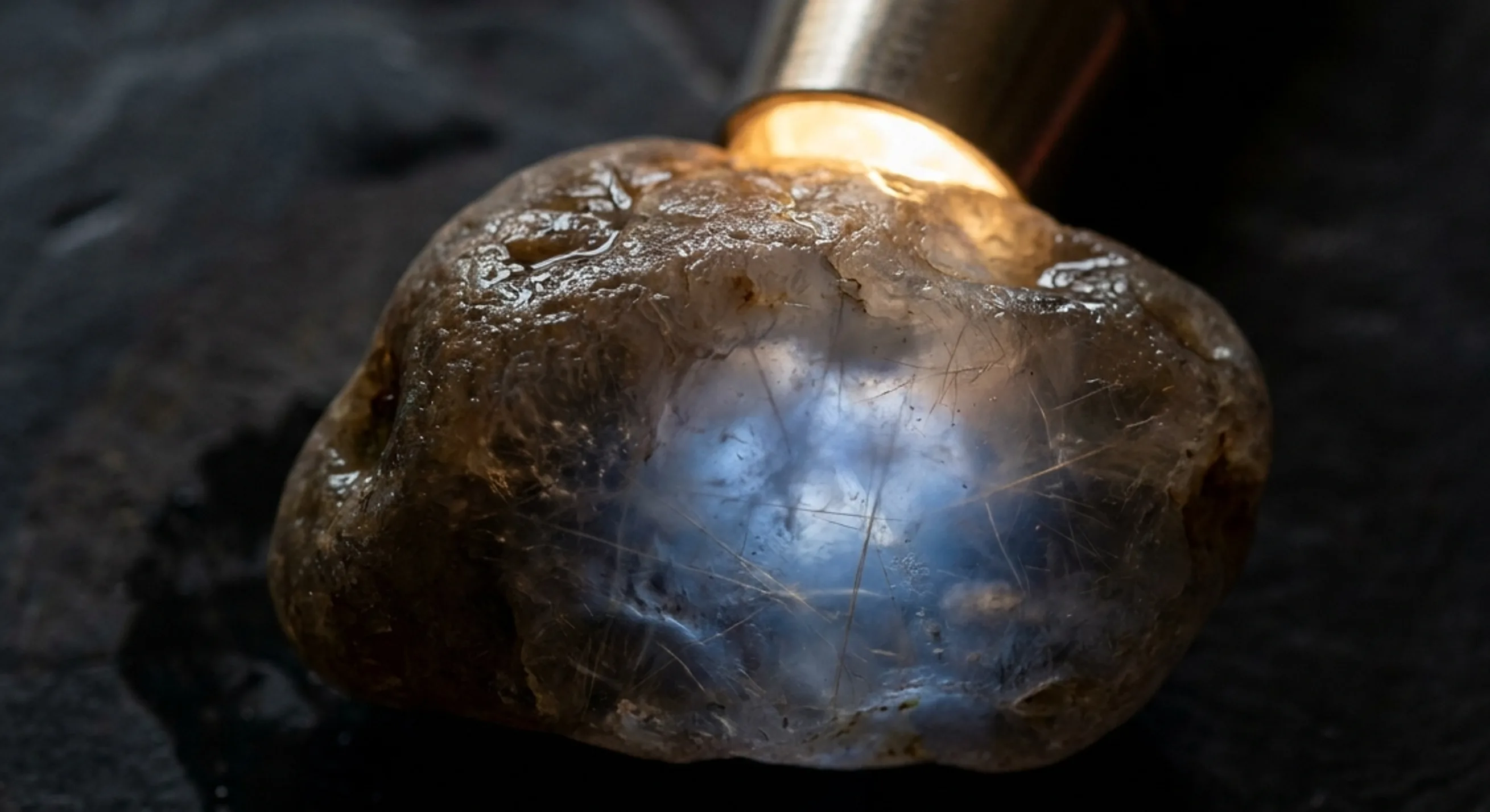 Brown rough sapphire pebble backlit by a torch revealing faint blue glow inside