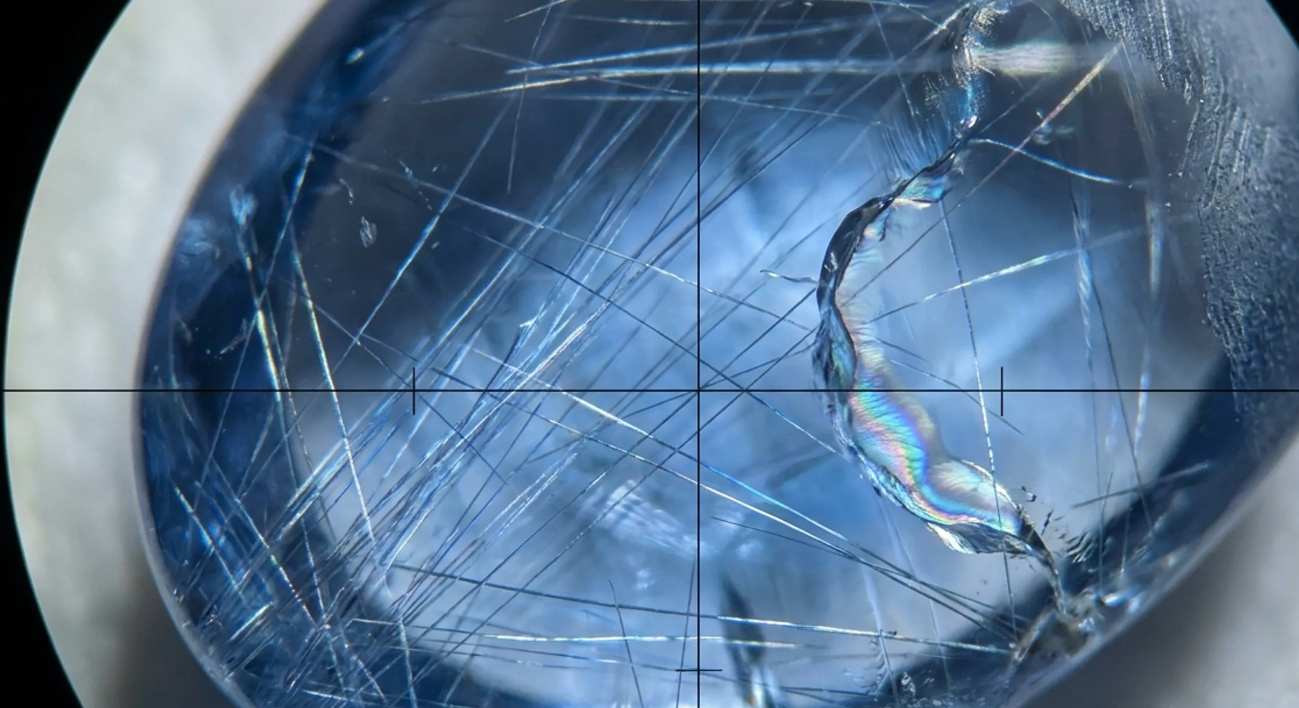 Magnified interior of a blue sapphire revealing fine rutile silk needles and a healed fissure inclusion