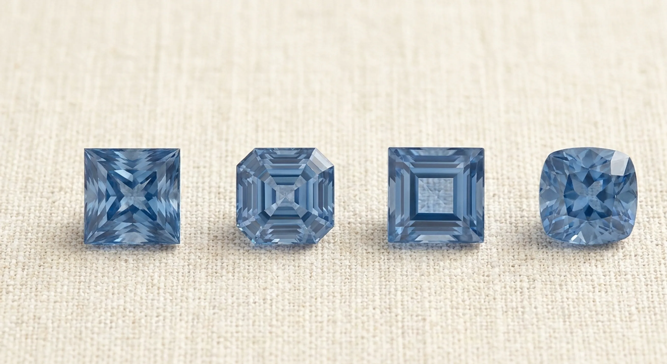 Four square blue sapphires in a row on linen: princess, Asscher, carré and square cushion cuts