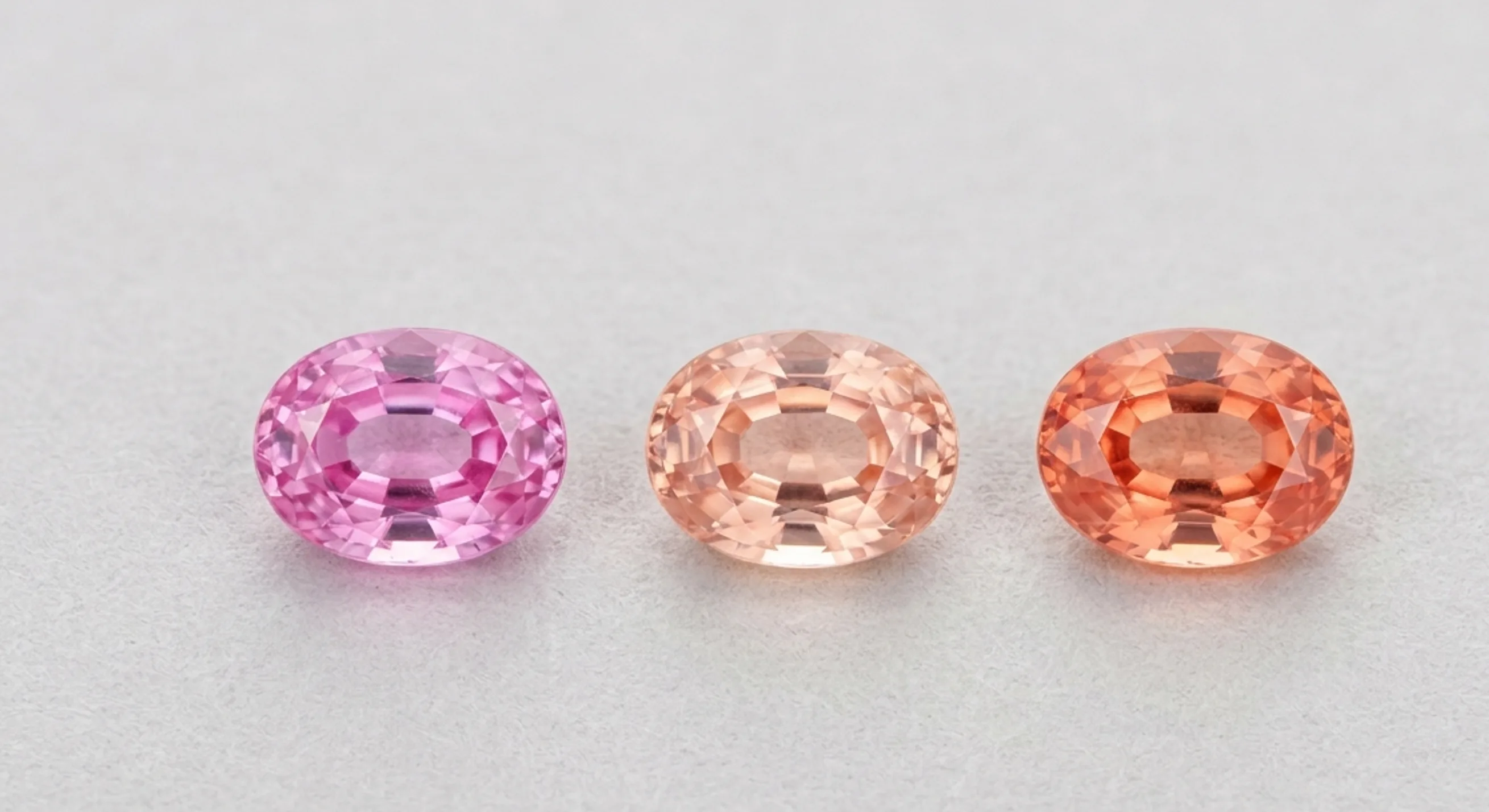Three loose sapphires in a row comparing cool pink, soft peach, and salmon padparadscha tones