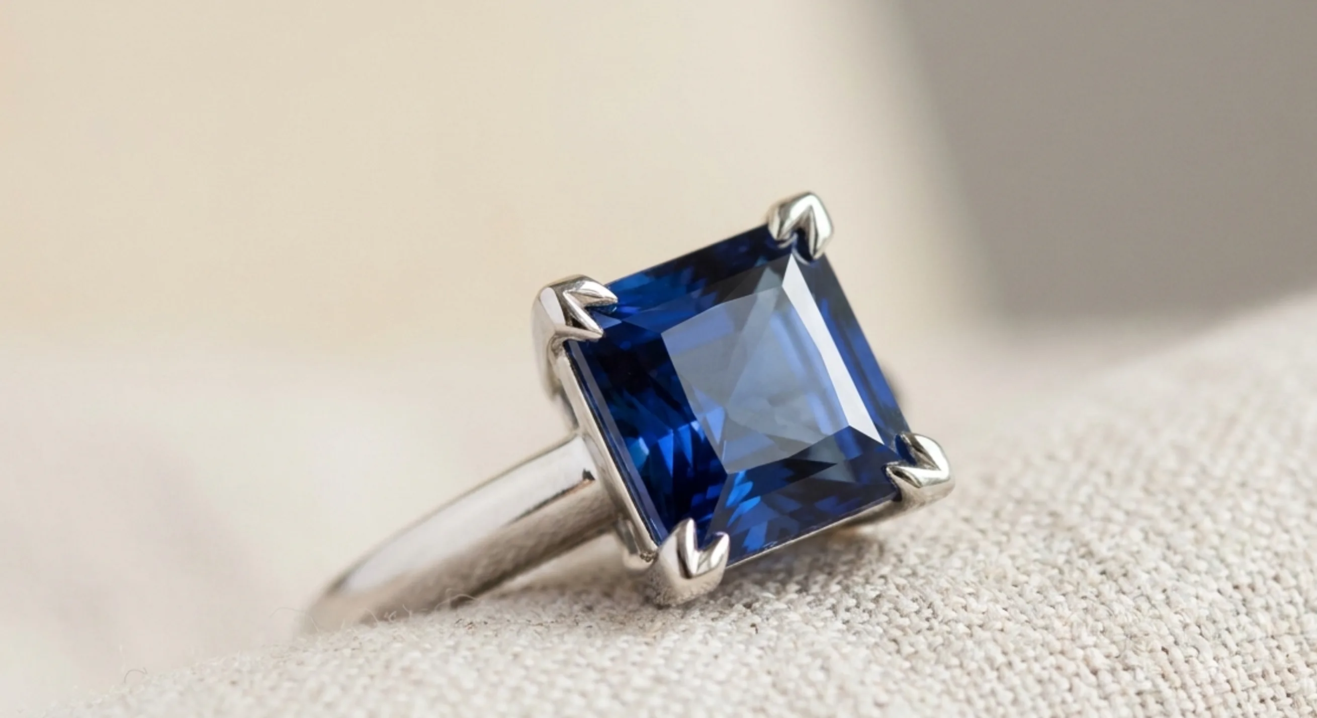 Princess cut blue sapphire held by V-prongs at each corner in a white-metal ring setting