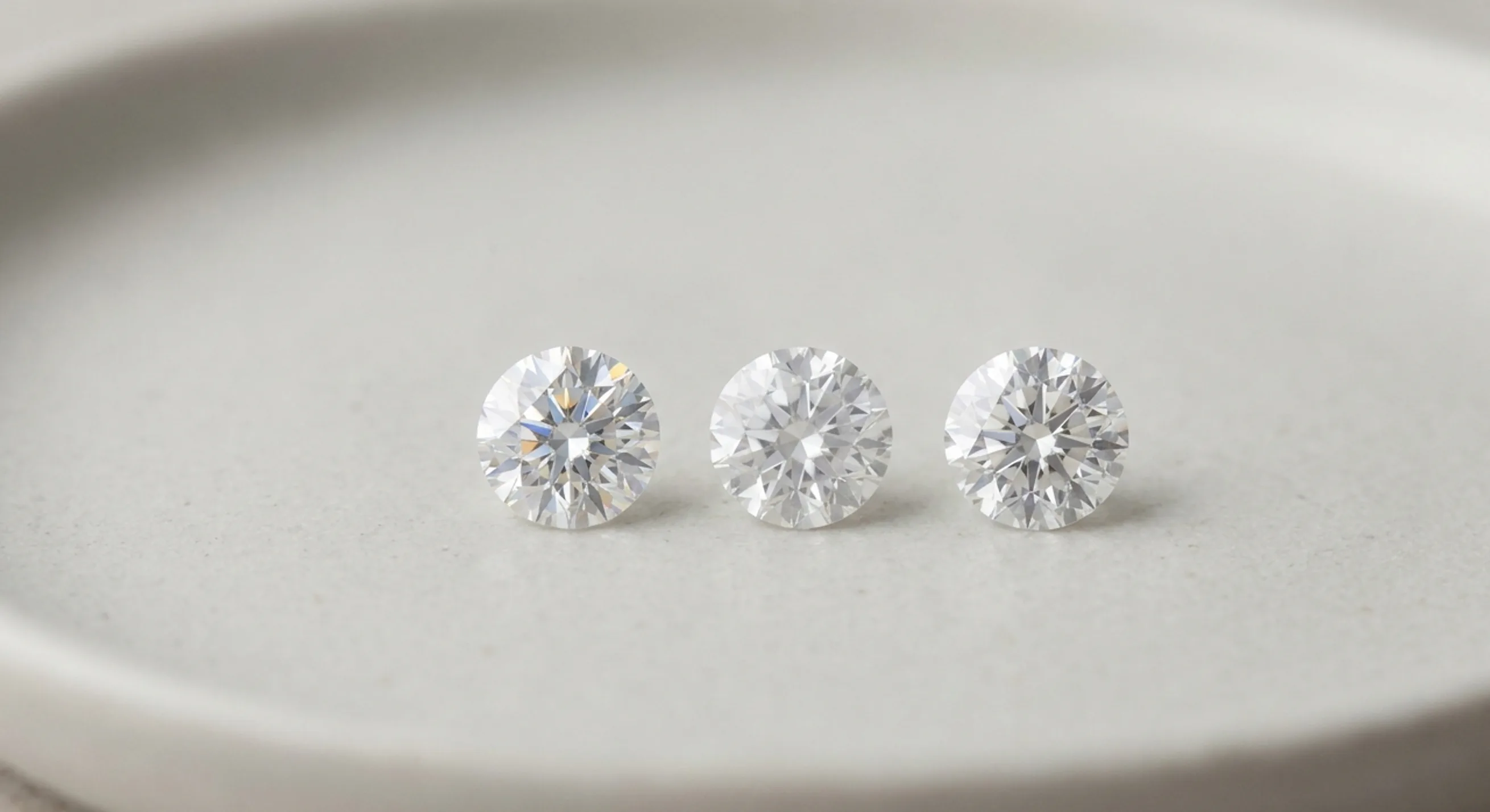 Moissanite, white sapphire, and lab-grown diamond lined up for comparison on a matte grey surface