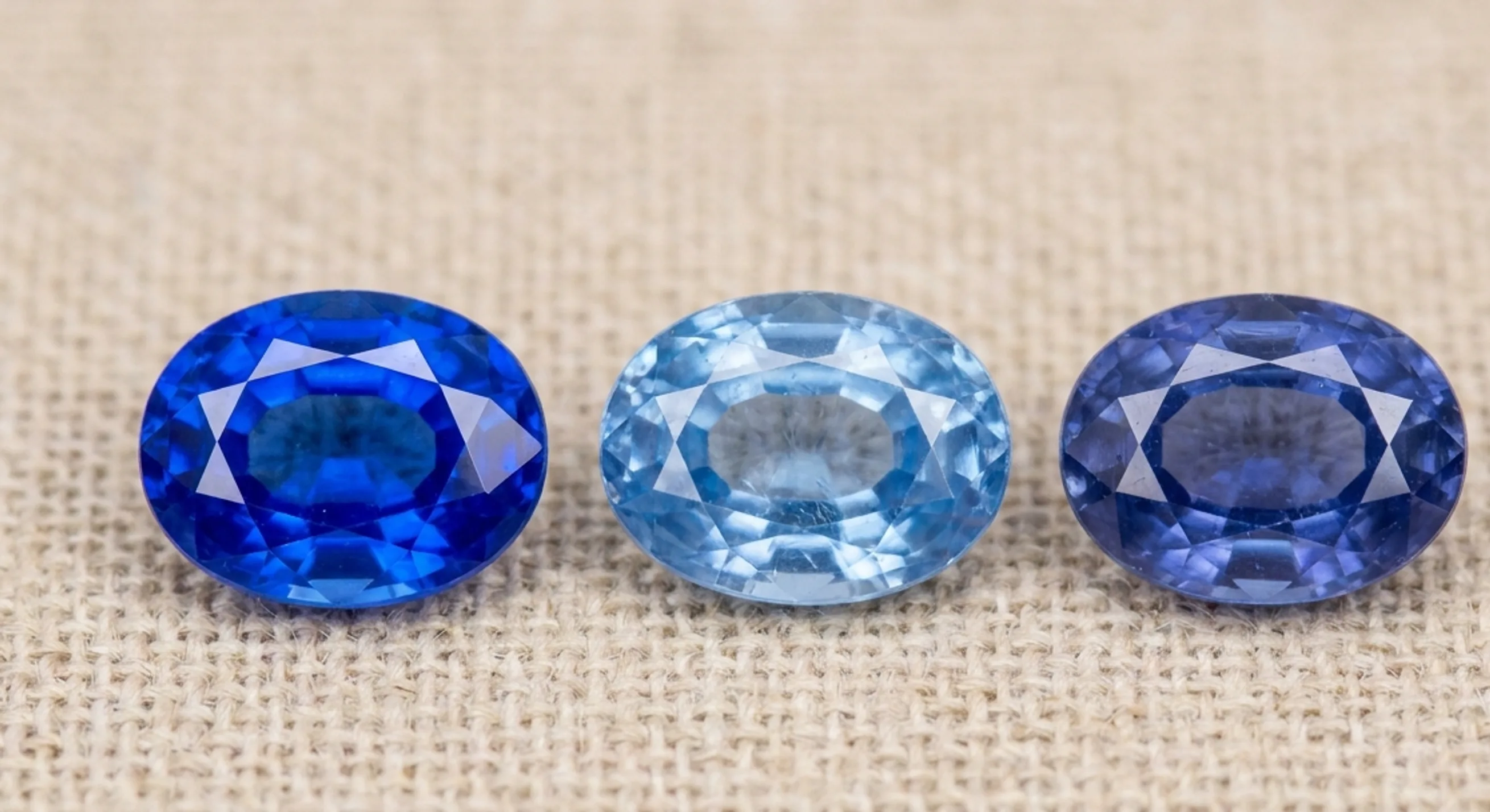 Three loose blue sapphires of differing colour intensity arranged on linen for comparison