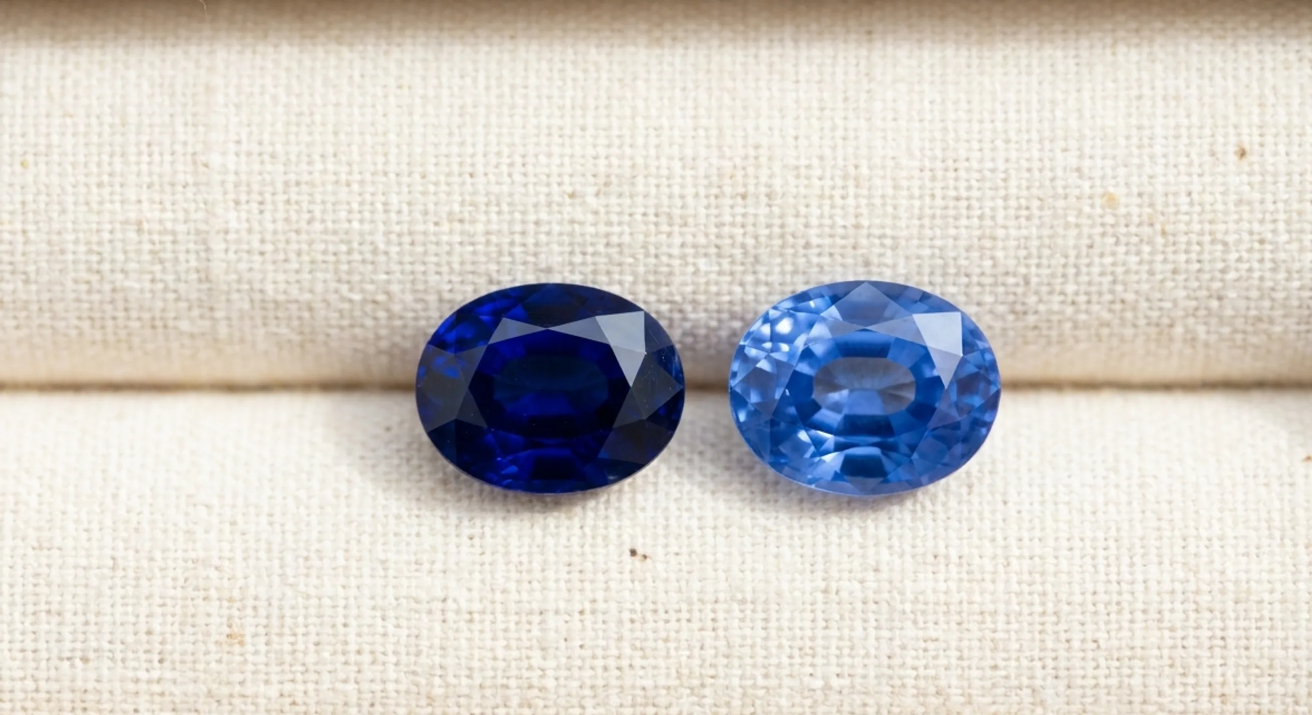 A deep royal blue sapphire and a brighter cornflower blue sapphire side by side on white linen