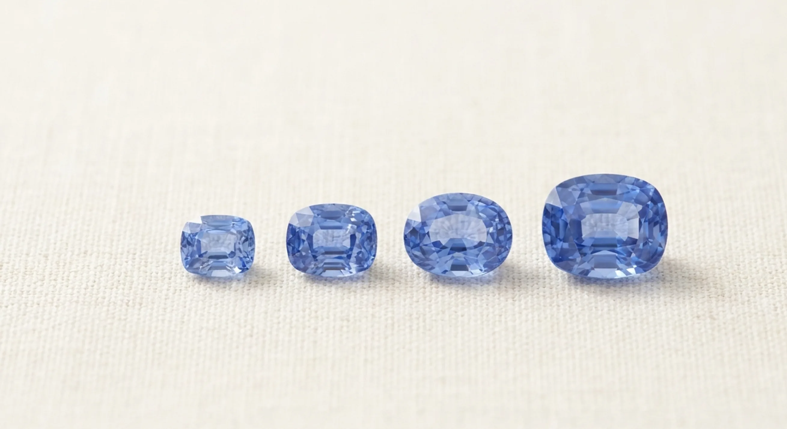 Four cornflower-blue sapphires of increasing size lined up on cream linen