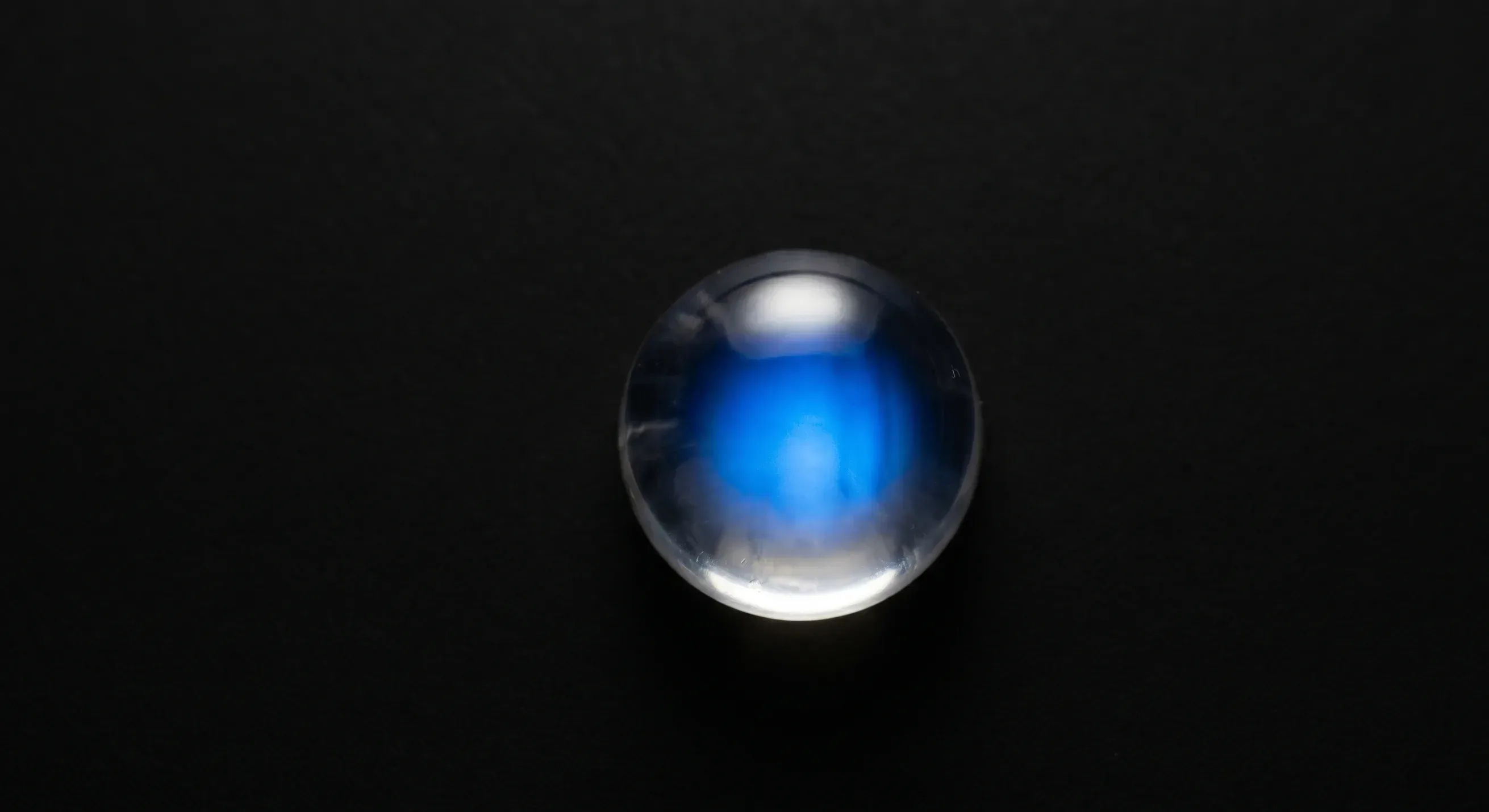 A colorless Ceylon moonstone cabochon under direct lighting showing a bright centered blue adularescence