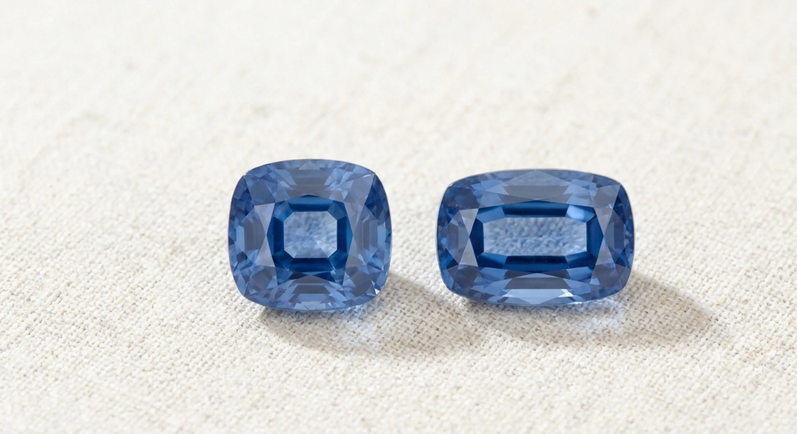 A square cushion sapphire next to an elongated rectangular cushion sapphire on oatmeal linen