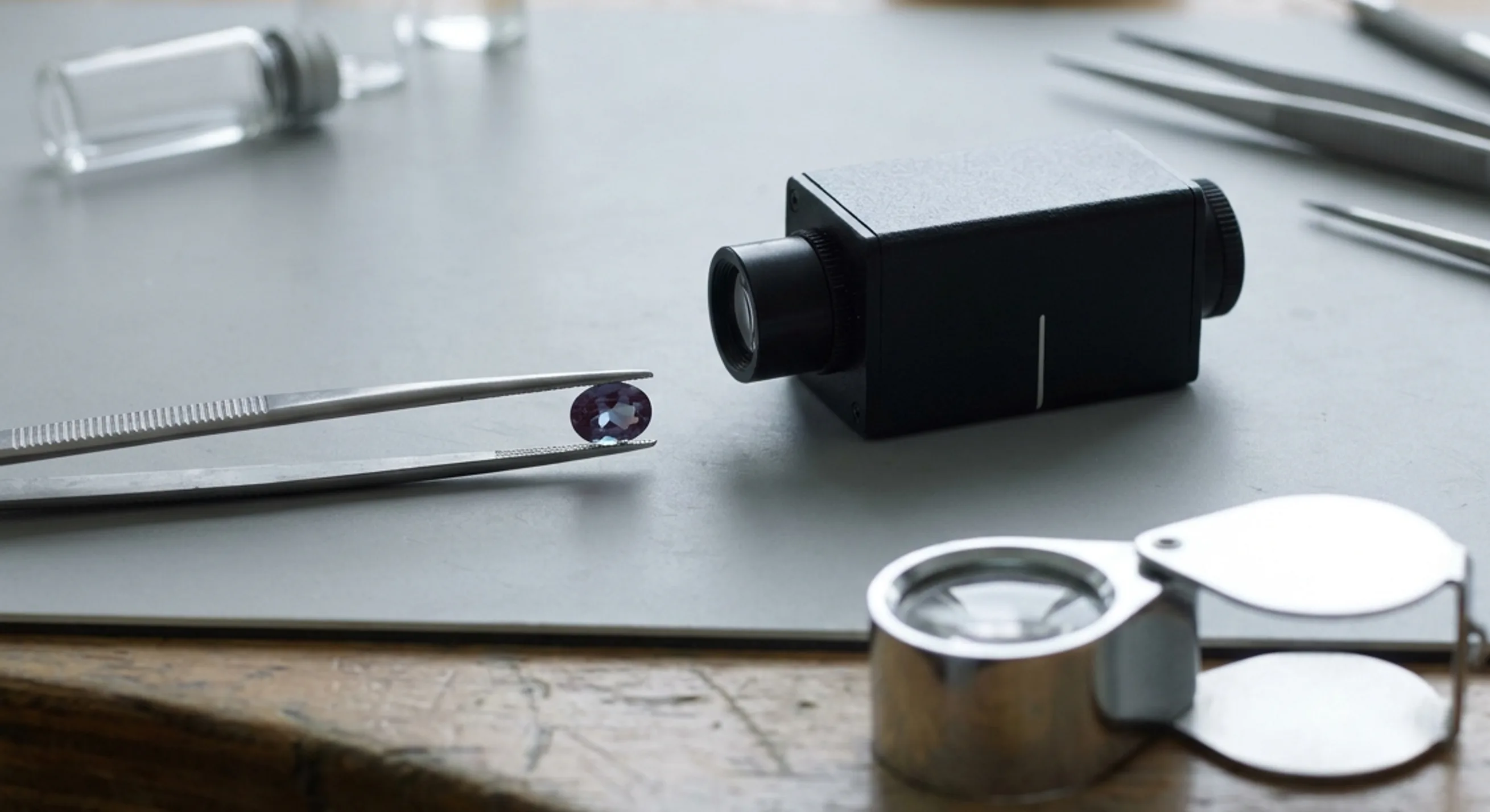 Alexandrite held in tweezers beside a loupe and spectroscope on a lab bench