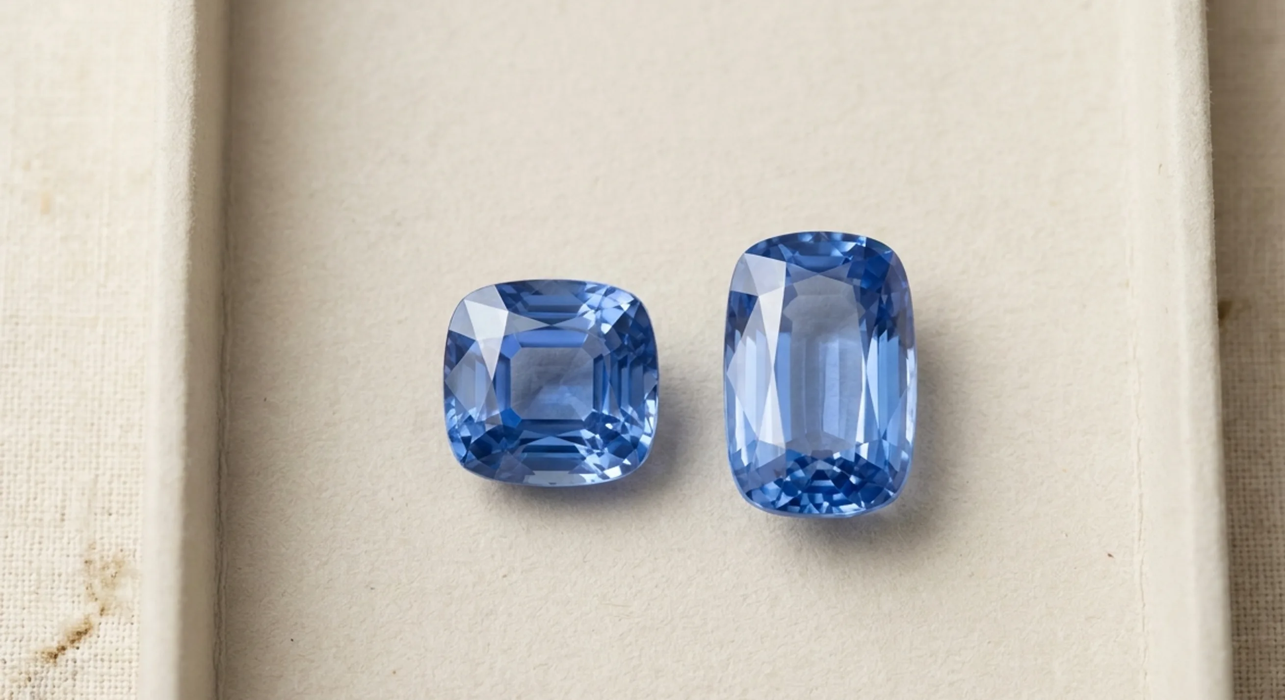 A square cushion sapphire beside an elongated cushion sapphire on pale paper, showing two length-to-width ratios