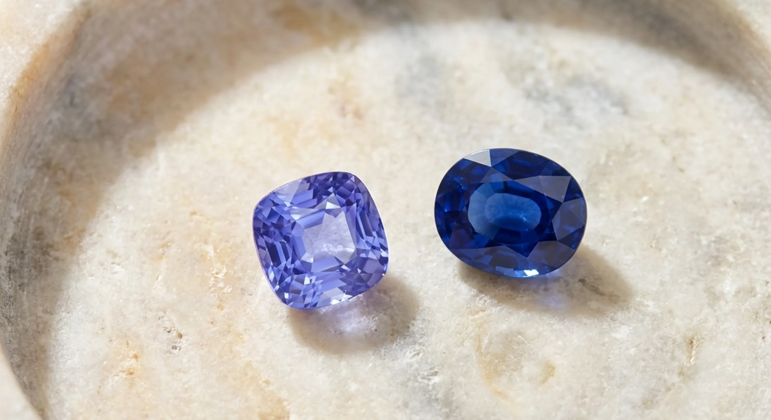 A bright violetish blue Ceylon sapphire next to a deeper royal blue sapphire on a pale stone tray