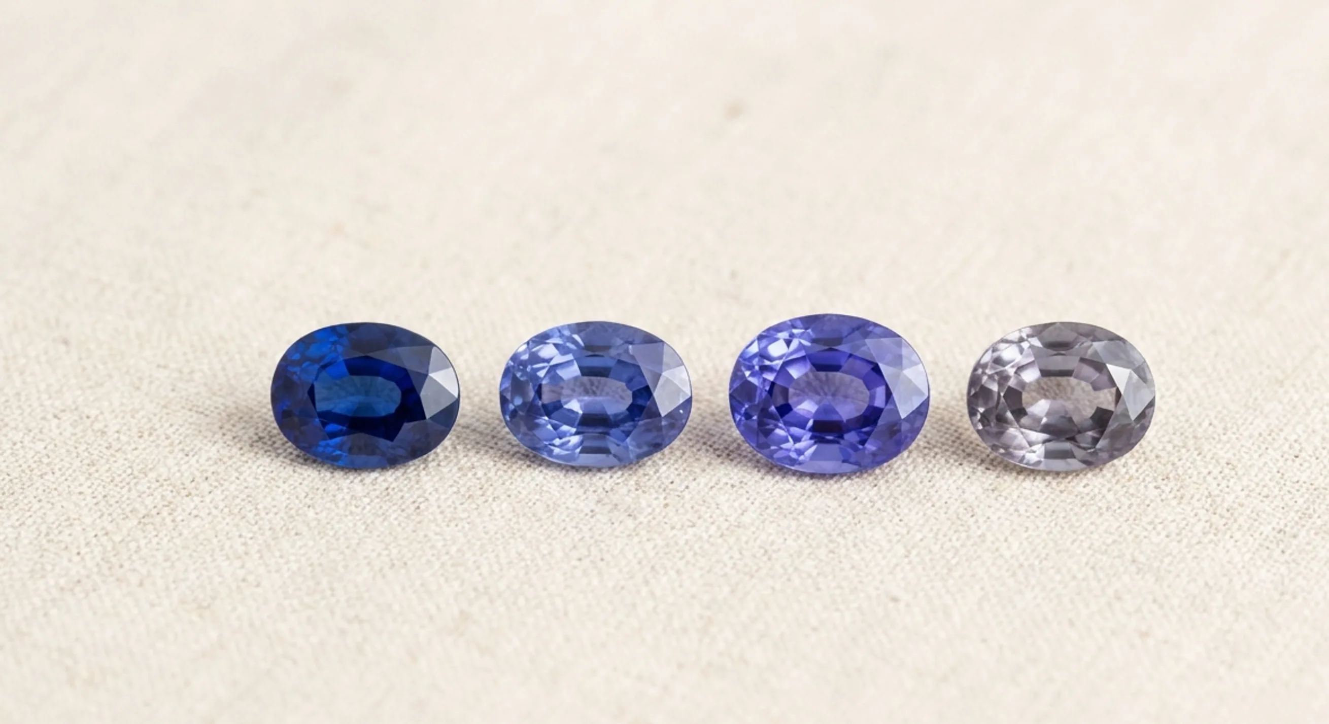 Four loose sapphires on linen ranging from pure blue and violetish blue to near-purple and greyish lavender
