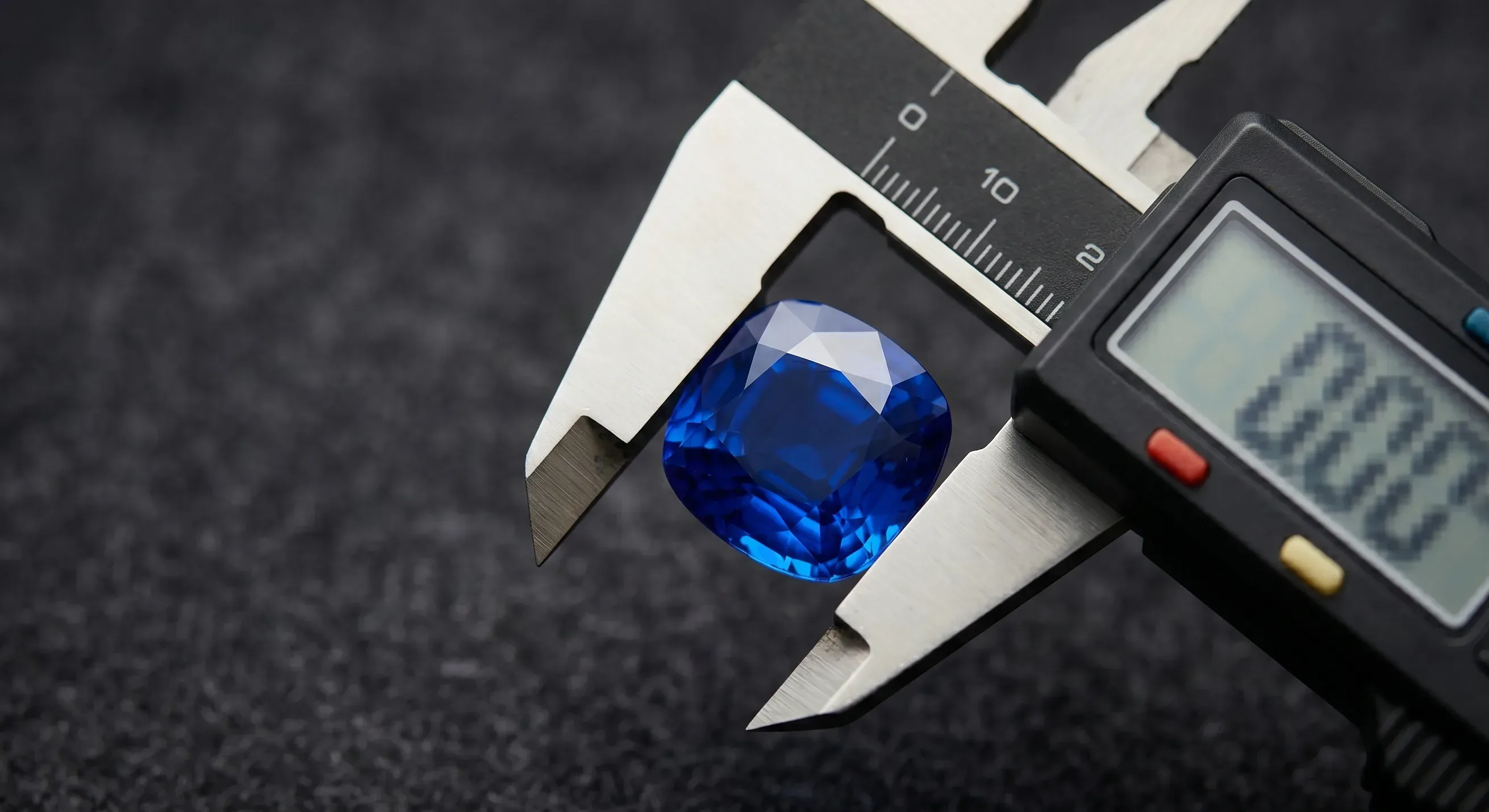 Macro close-up of a faceted Ceylon sapphire being measured with a digital caliper against a dark fabric background, showing the millimeter reading on the caliper display.