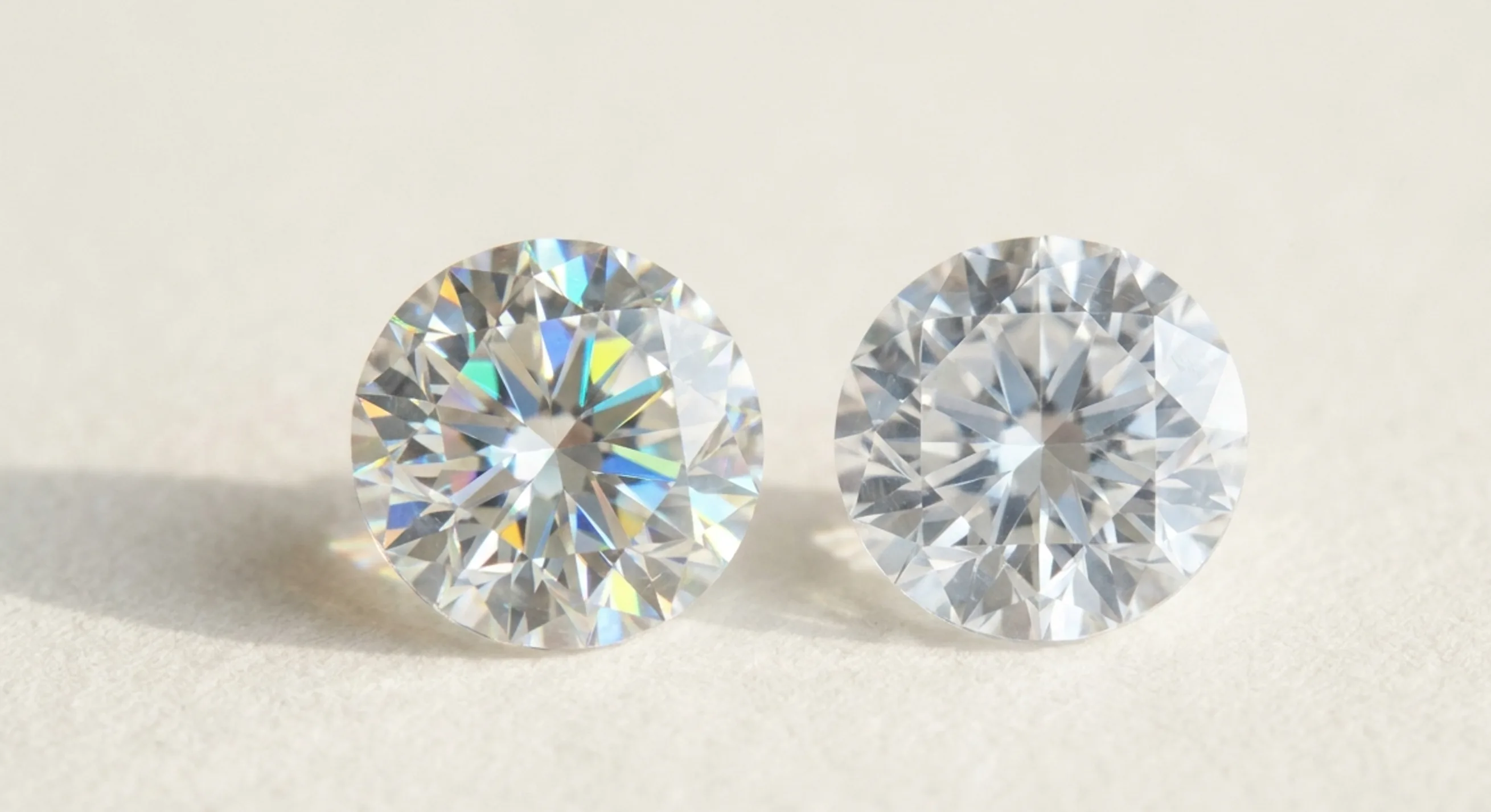 A colorless zircon showing rainbow fire beside a crisp, icy white sapphire on white paper