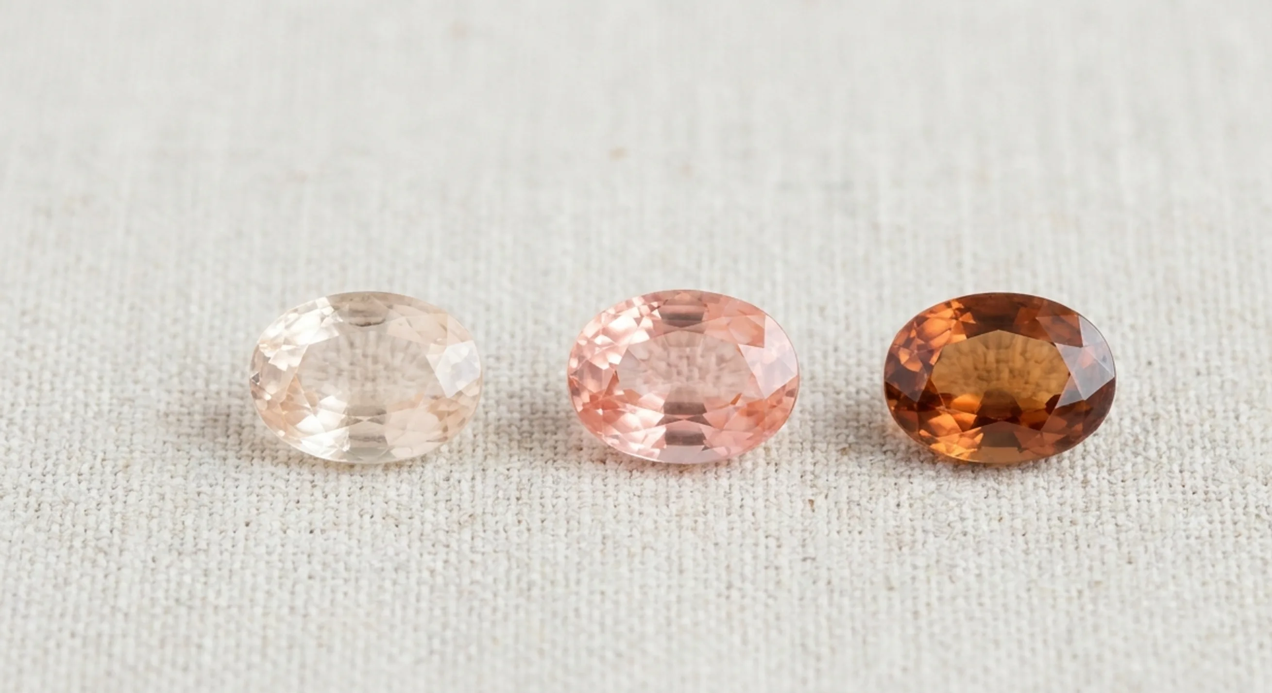 Three salmon-coloured sapphires on linen, going from too light, to an ideal pastel tone, to too dark with a brownish edge