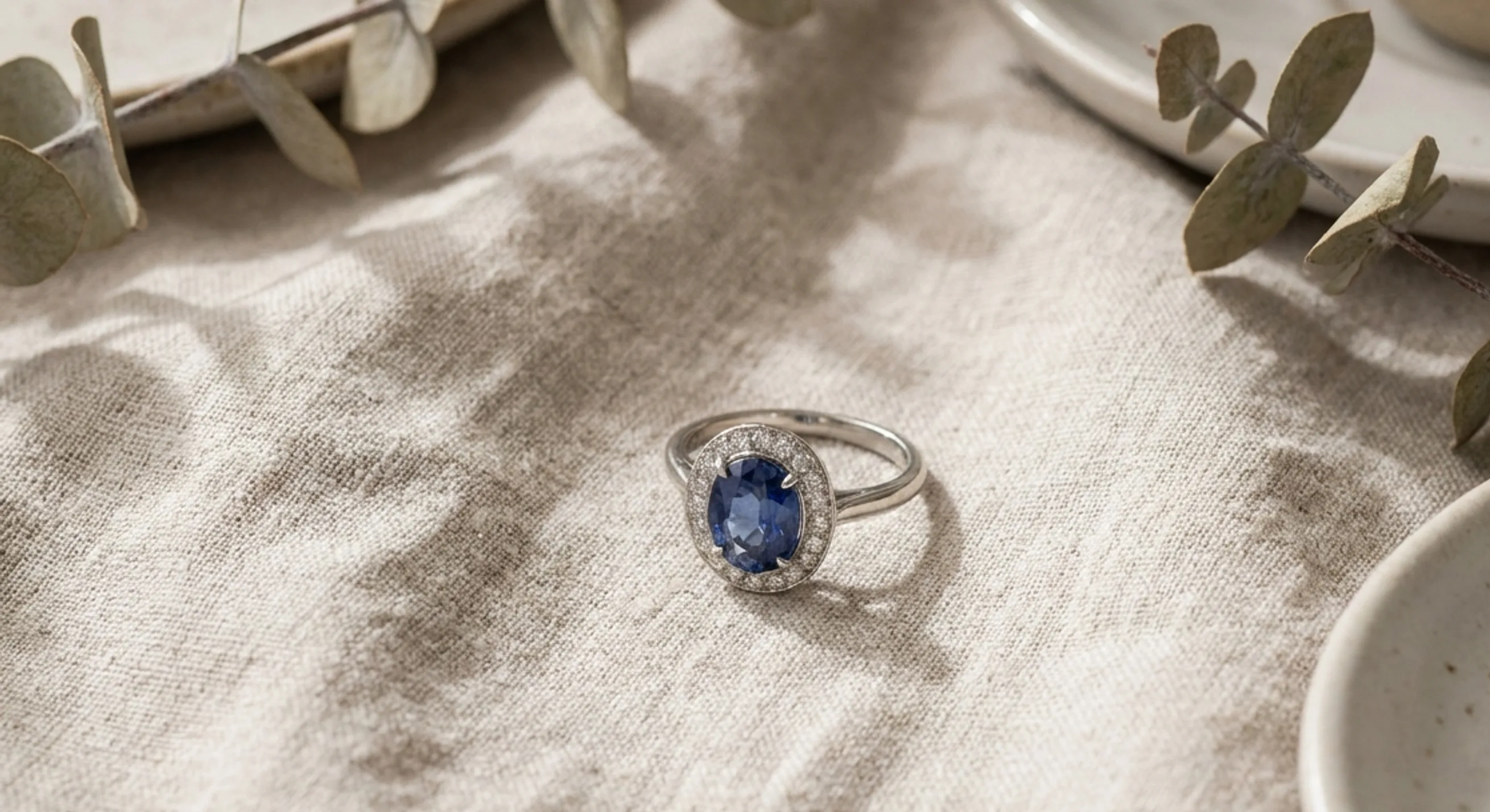Blue Ceylon sapphire ring framed by a pavé diamond halo on oatmeal linen