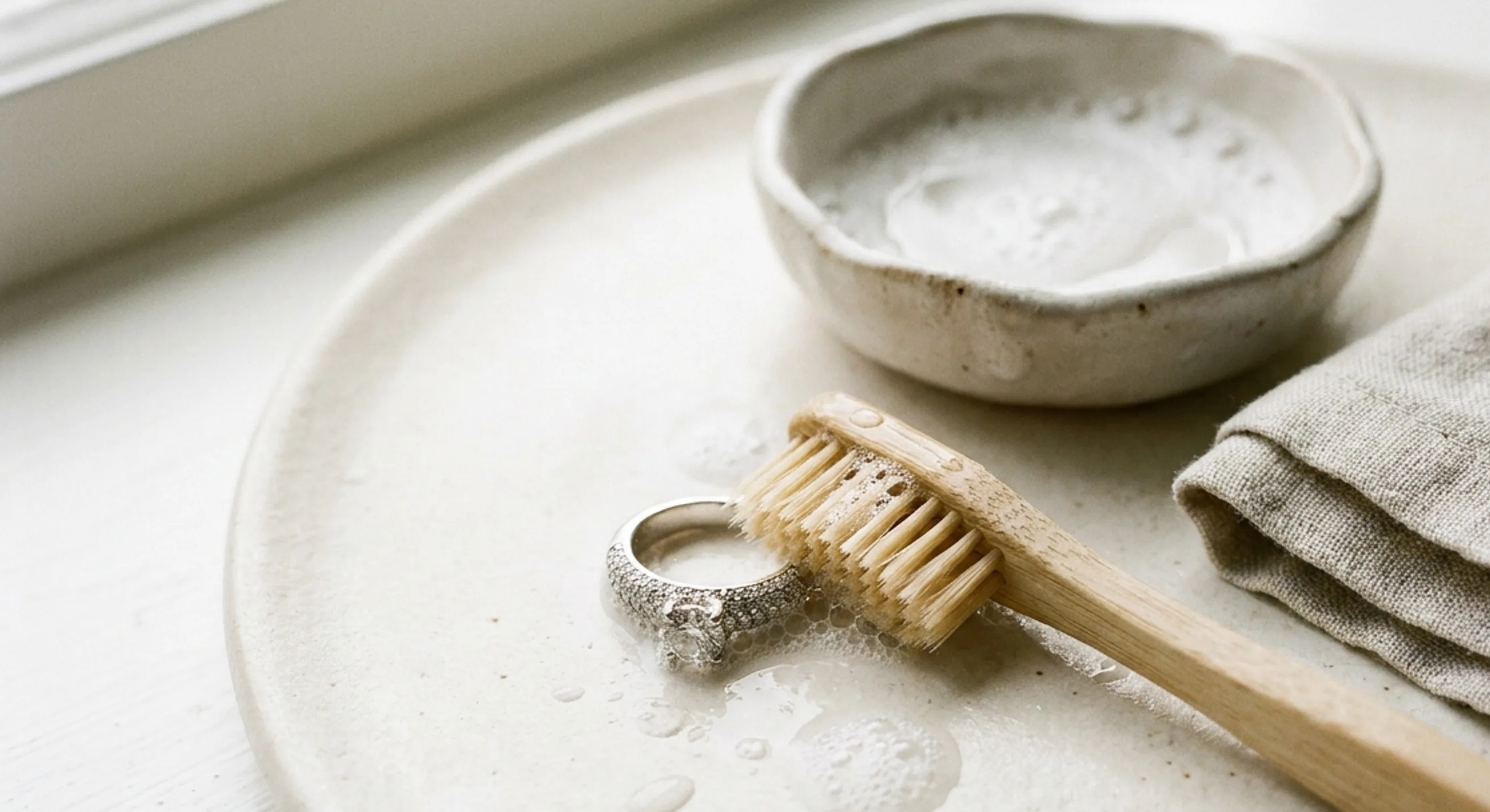 Pavé ring beside a soft brush, soapy water dish and lint-free cloth for cleaning
