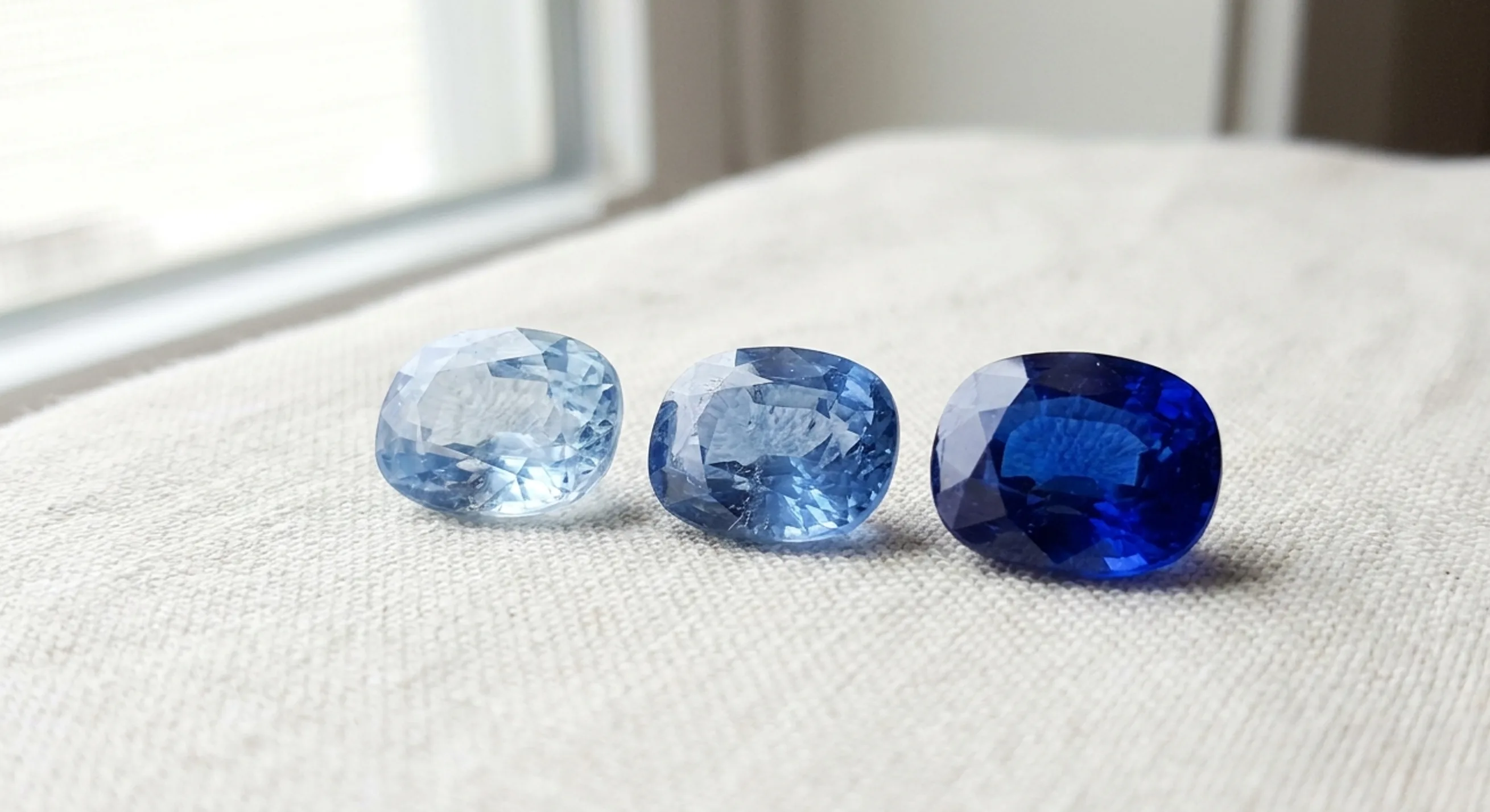 Three loose sapphires in a row showing a range from pale blue to deep vivid blue